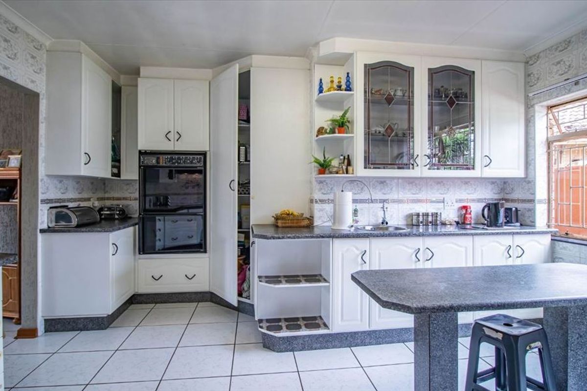 A functional kitchen featuring white cabinetry, double wall ovens, laminate countertops, tiled backsplash, and ceramic floor tiles with a breakfast nook area.