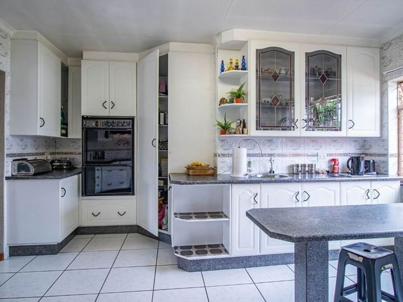 A functional kitchen featuring white cabinetry, double wall ovens, laminate countertops, tiled backsplash, and ceramic floor tiles with a breakfast nook area.