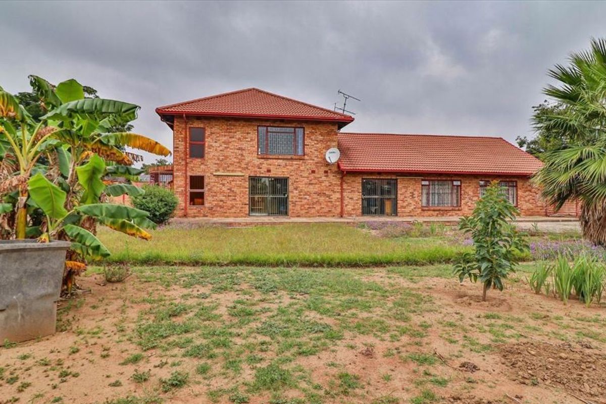 Rear view of a double-story face brick house featuring a tiled roof, security gates, and a large garden area.