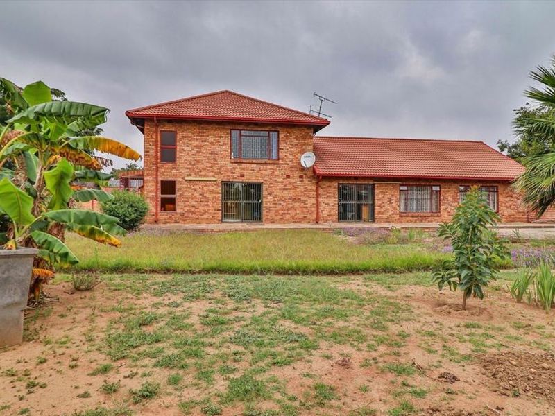 Rear view of a double-story face brick house featuring a tiled roof, security gates, and a large garden area.