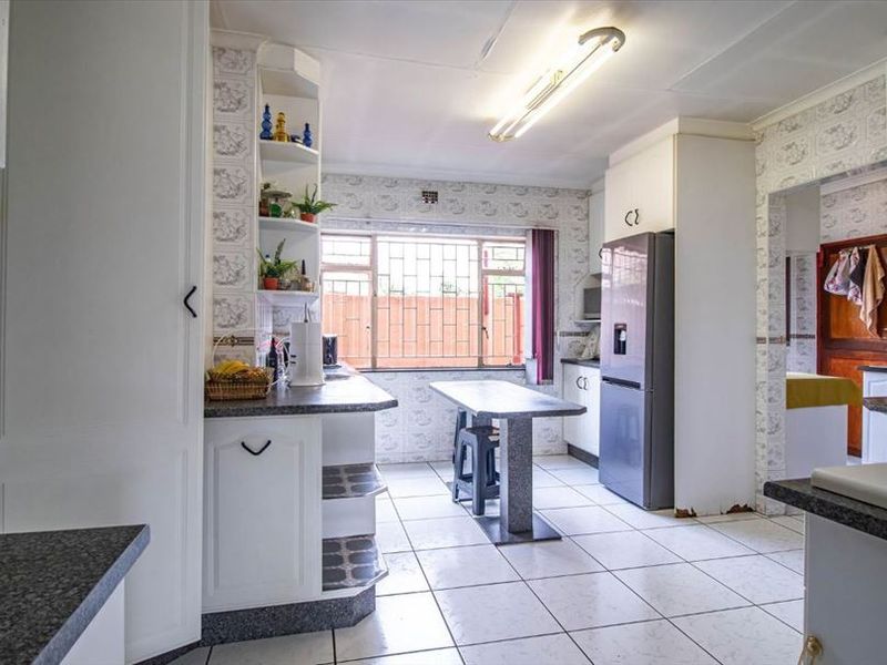A functional kitchen featuring built-in cabinetry, laminate countertops, and ceramic floor tiles, with security bars installed on the window.