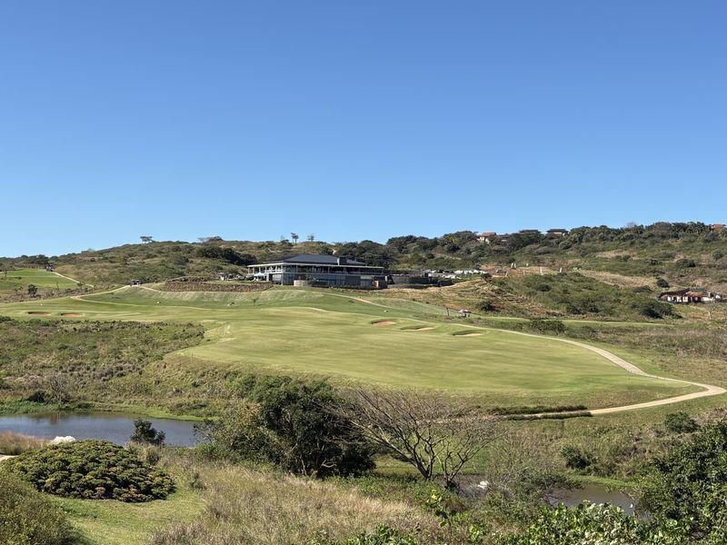 A scenic view of a well-maintained golf course featuring rolling green fairways, a water hazard, and a clubhouse situated on the hillside.
