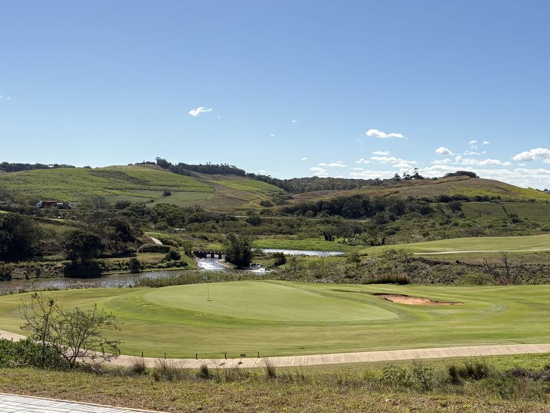 A scenic view overlooking a well-maintained golf course with rolling hills and a water feature in the background.