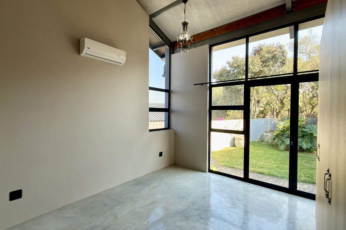 Bright bedroom featuring polished concrete floors, exposed structural beams, and large glass doors opening to a private garden.