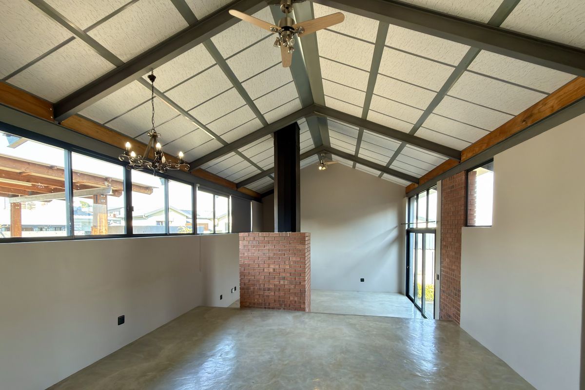 Spacious living area featuring a vaulted ceiling with exposed steel beams, polished concrete floors, and a central brick fireplace.