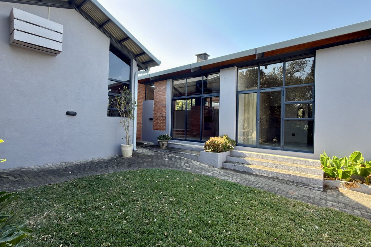 A well-maintained rear exterior view featuring a paved patio, landscaped lawn, and large glass sliding doors providing seamless indoor-outdoor flow.