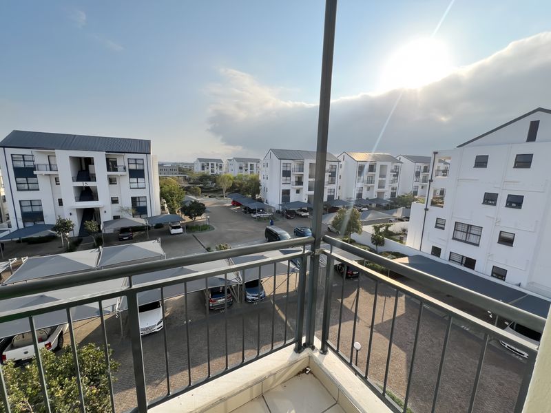 A view from a balcony overlooking a residential apartment complex with paved parking areas and covered carports.