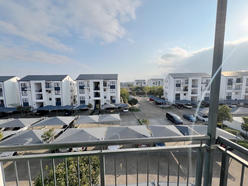 Elevated view overlooking the apartment complex grounds, featuring paved parking areas with shade cloth carports and surrounding residential buildings.