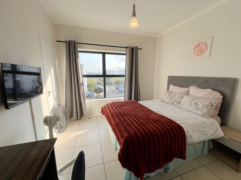 A well-lit bedroom featuring neutral tiled flooring, a large window with natural light, and a coved ceiling, providing a comfortable and functional living space.