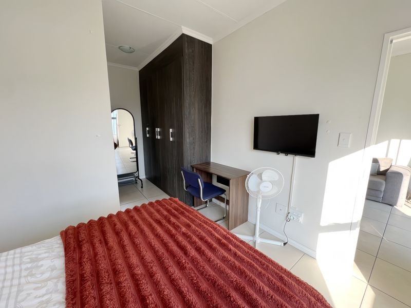A bedroom featuring tiled flooring and a dark wood built-in wardrobe, offering a functional layout with wall-mounted television and desk space.