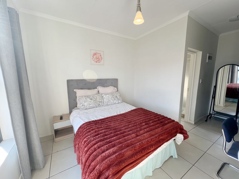 A well-lit bedroom featuring neutral tiled flooring, a simple pendant light, and direct access to an en-suite bathroom.