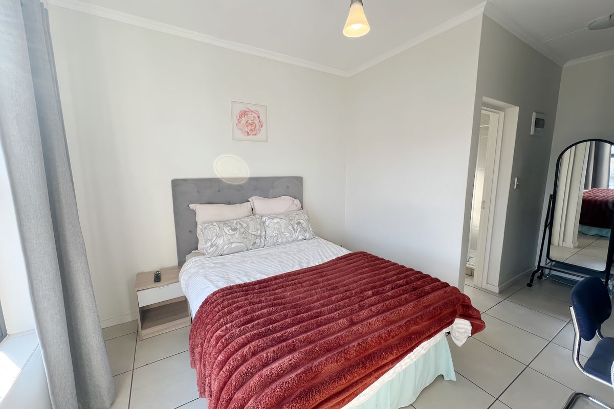 A well-lit bedroom featuring neutral tiled flooring, a simple pendant light, and direct access to an en-suite bathroom.
