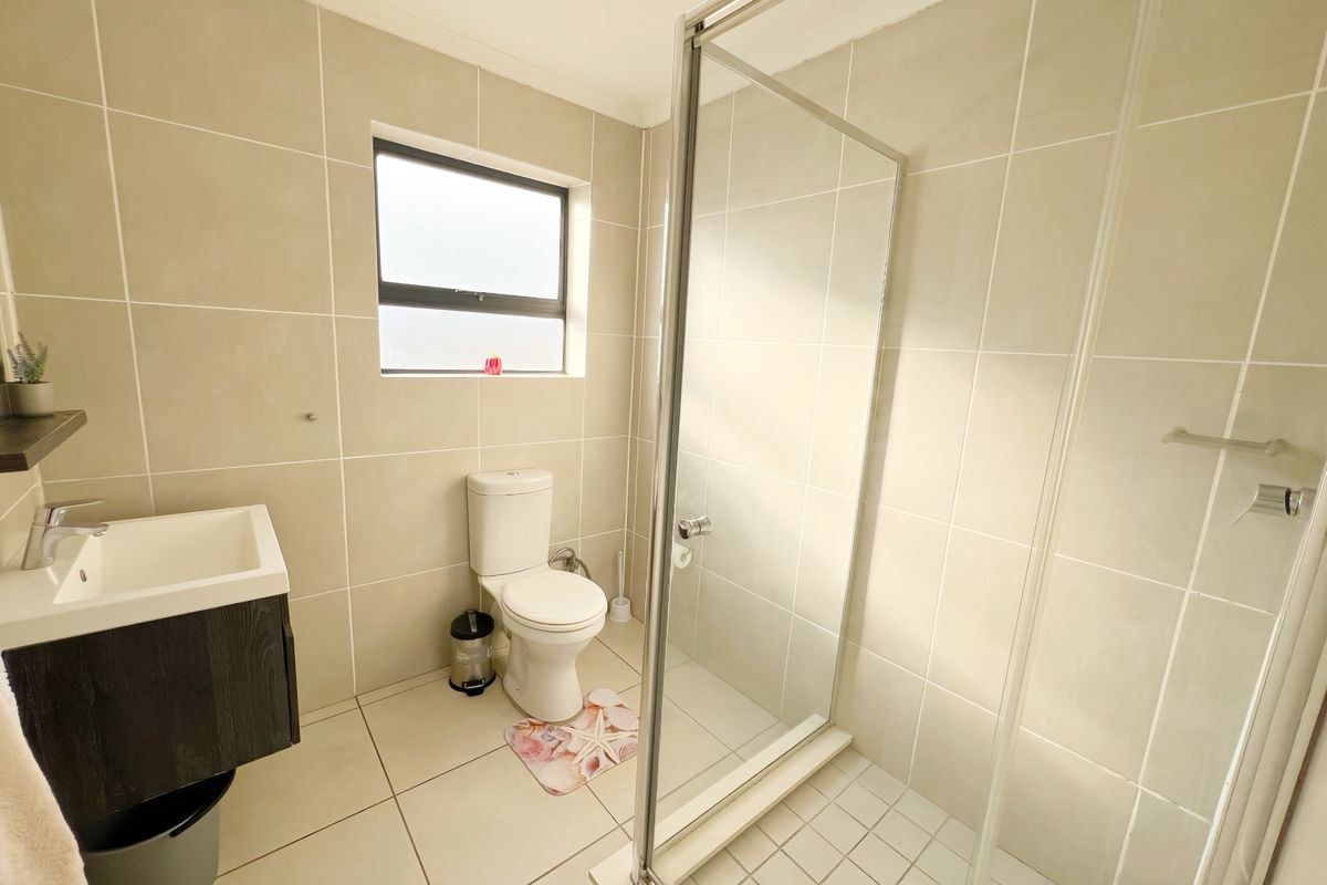A modern bathroom featuring a glass-enclosed shower, wall-mounted vanity, and neutral floor-to-ceiling tiling.