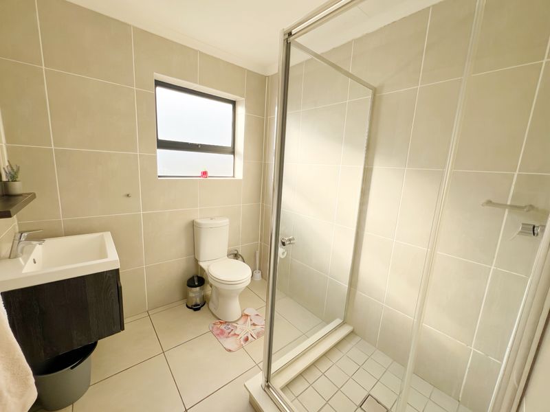 A modern bathroom featuring a glass-enclosed shower, wall-mounted vanity, and neutral floor-to-ceiling tiling.