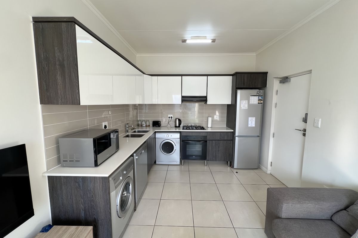 Modern open-plan kitchen featuring high-gloss cabinetry, integrated appliances, tiled flooring, and a neutral backsplash, seamlessly connected to the living area.