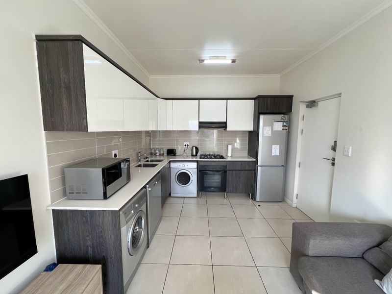 Modern open-plan kitchen featuring high-gloss cabinetry, integrated appliances, tiled flooring, and a neutral backsplash, seamlessly connected to the living area.