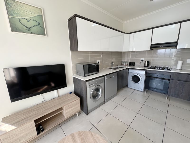 Modern open-plan kitchen featuring high-gloss cabinetry, integrated appliances, tiled flooring, and a sleek tiled backsplash, seamlessly connected to the living area.
