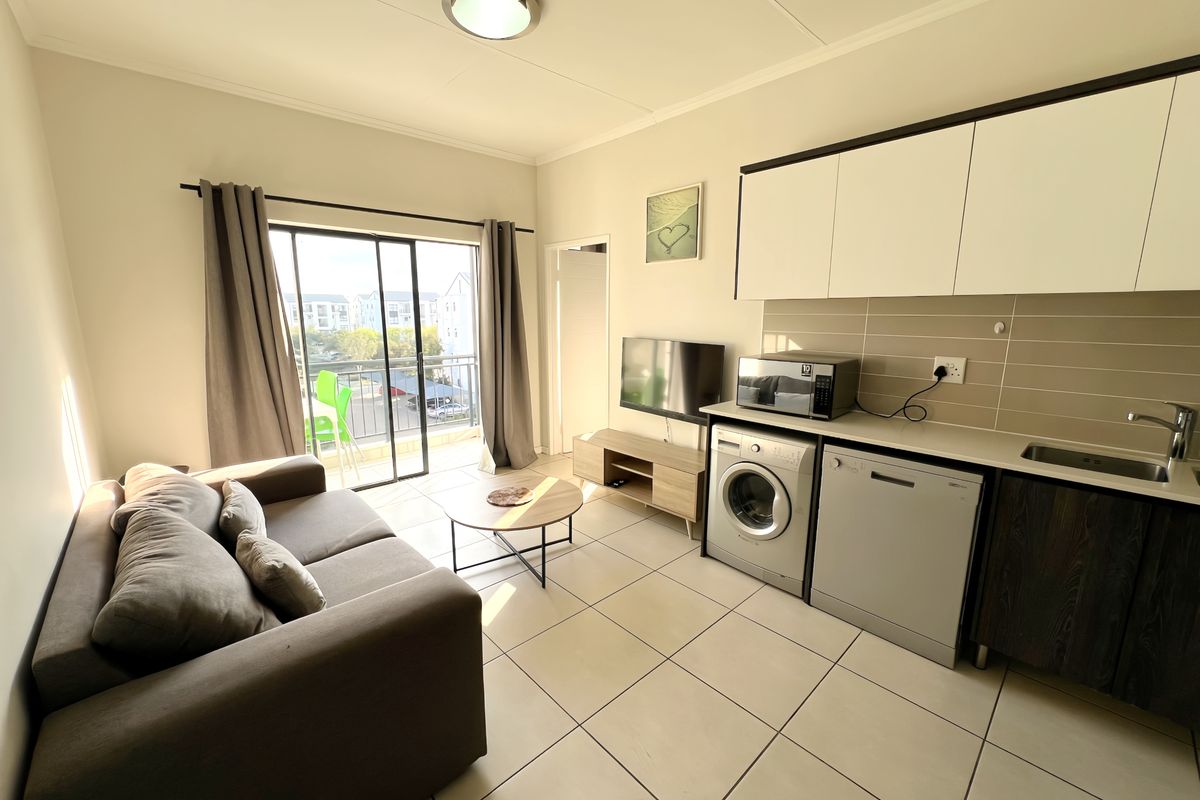 Open-plan living area featuring a compact kitchen with built-in cabinetry, tiled flooring, and a sliding door leading to a balcony.