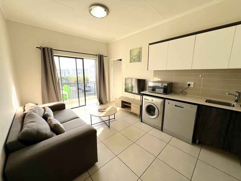 Open-plan living area featuring a compact kitchen with built-in cabinetry, tiled flooring, and a sliding door leading to a balcony.