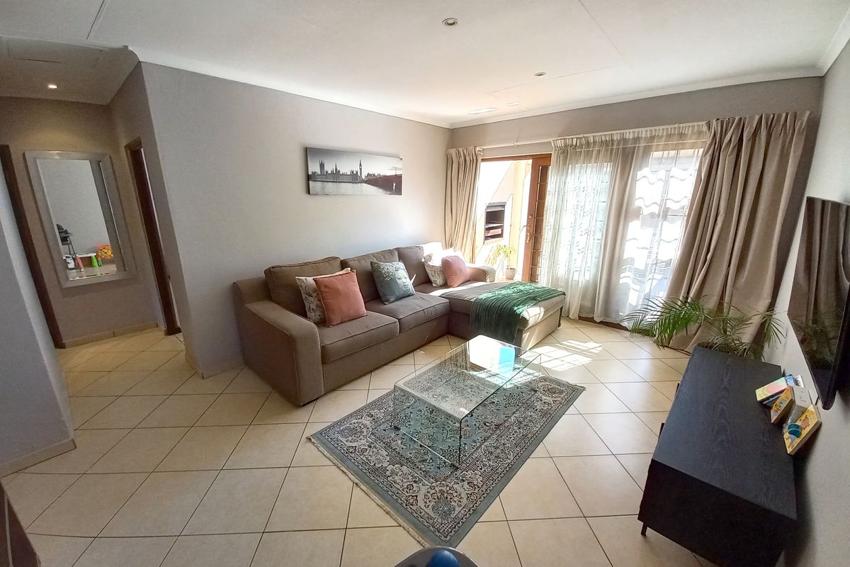 A bright and spacious living room featuring neutral tiled flooring, recessed lighting, and a sliding glass door providing access to the outdoor area.