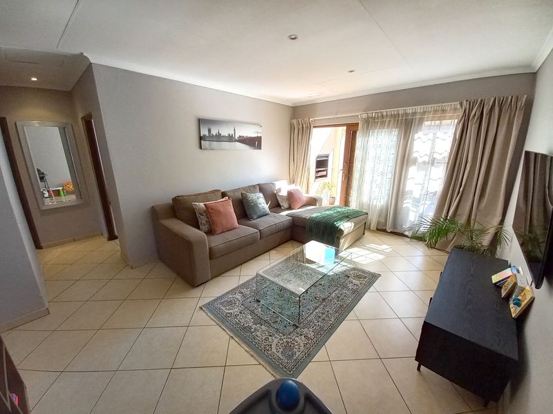 A bright and spacious living room featuring neutral tiled flooring, recessed lighting, and a sliding glass door providing access to the outdoor area.