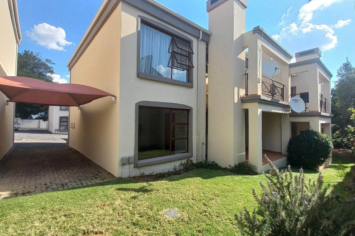 Rear view of the apartment building featuring a paved driveway with a shade sail carport, a balcony, and established garden space.