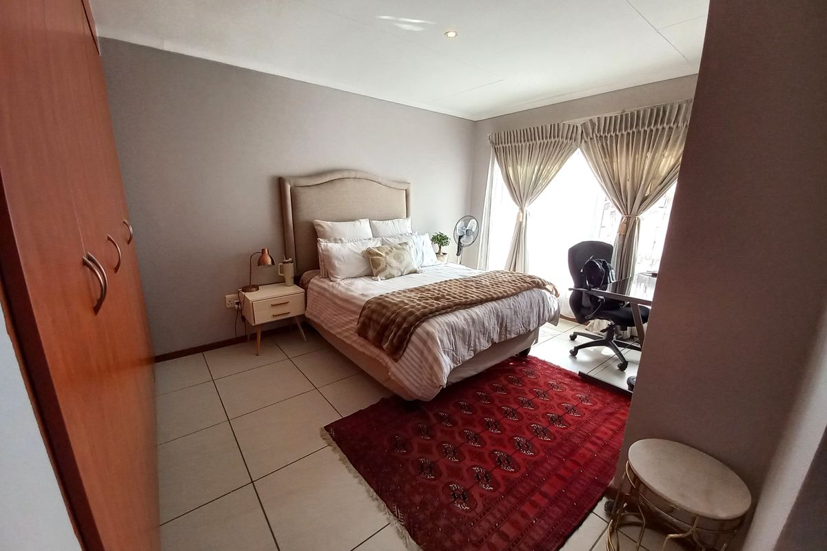 A well-maintained bedroom featuring neutral wall tones, large format floor tiles, and a spacious built-in wardrobe with wood-finish cabinetry.