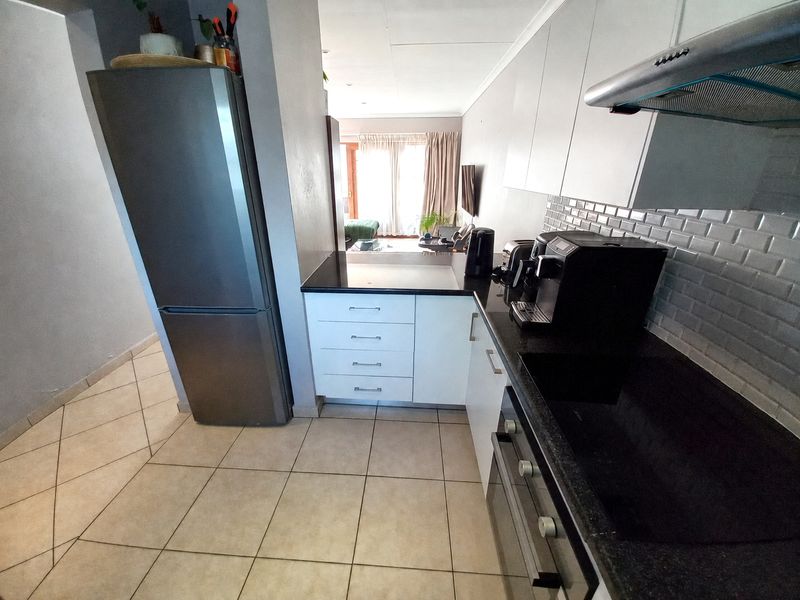 Modern kitchen featuring white cabinetry, dark stone countertops, subway tile backsplash, built-in oven, and extractor fan, with tiled flooring throughout.