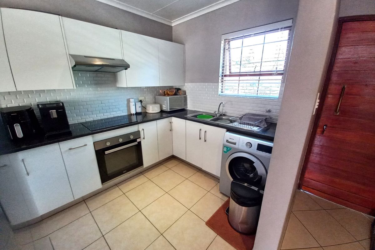 A well-maintained kitchen featuring white cabinetry, black granite countertops, subway tile backsplash, and integrated appliances, including a built-in oven and hob.