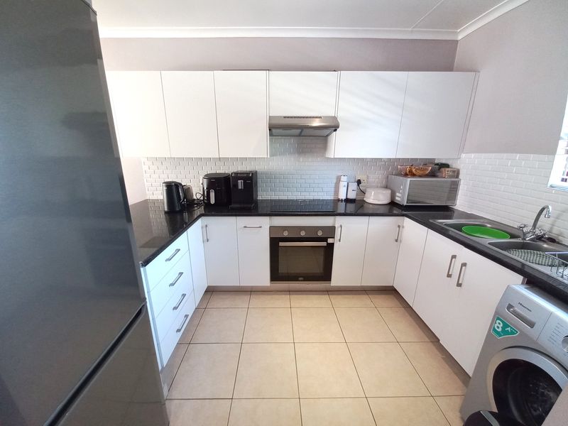 Modern kitchen featuring white cabinetry, black granite countertops, subway tile backsplash, and integrated appliances including an oven, hob, and extractor fan.