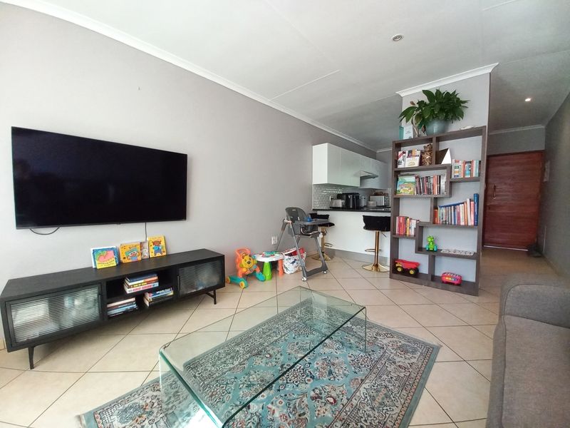 Open-plan living area featuring tiled flooring, a modern kitchen with breakfast counter, and neutral wall finishes.