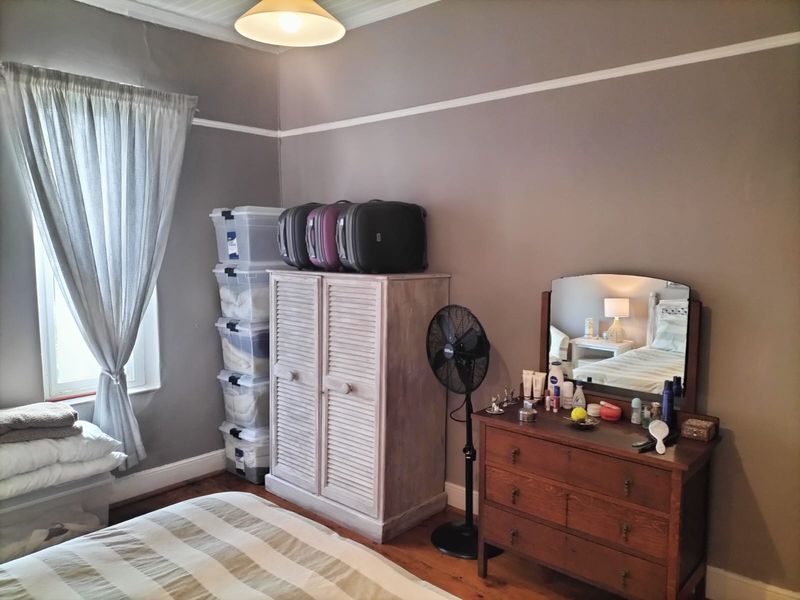 A bedroom featuring timber flooring and a classic picture rail, currently utilized with various storage solutions and furniture.