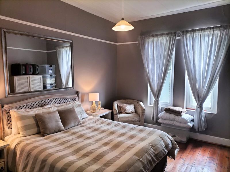 A cozy bedroom featuring original hardwood flooring, classic picture rails, and natural light through dual windows.