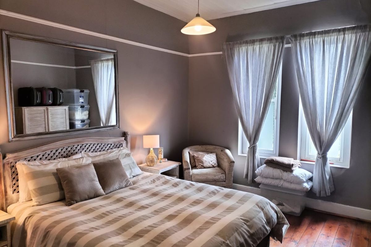A cozy bedroom featuring original hardwood flooring, classic picture rails, and natural light through dual windows.
