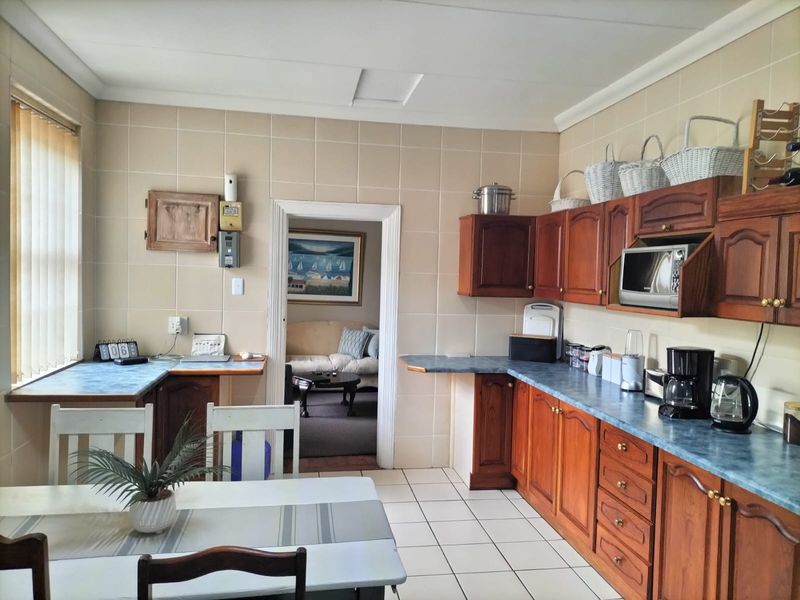 A functional kitchen featuring traditional wooden cabinetry, tiled wall finishes, and ample counter space, with an adjacent view into the living area.