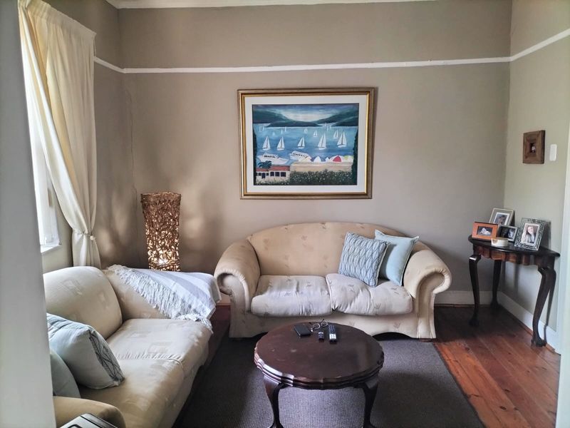 A cozy living room featuring original hardwood flooring, picture rails, and a visible wall crack requiring maintenance.