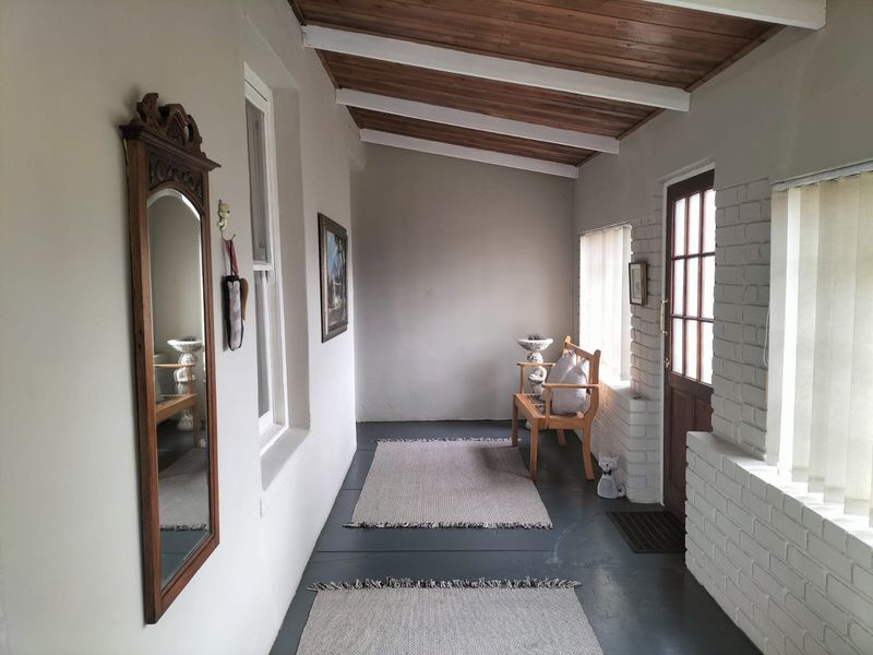 A covered patio area featuring exposed timber beams, painted brick walls, and a painted concrete floor, providing a bright and functional transition space.