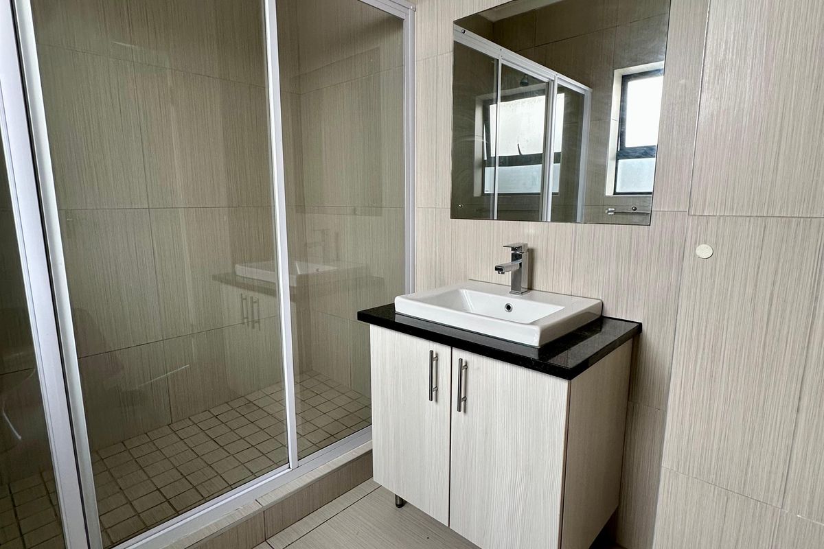 Modern bathroom featuring a glass shower enclosure, vanity cabinet with basin, and neutral wall and floor tiling.