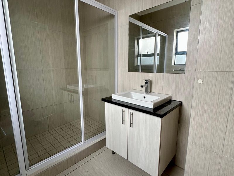 Modern bathroom featuring a glass shower enclosure, vanity cabinet with basin, and neutral wall and floor tiling.