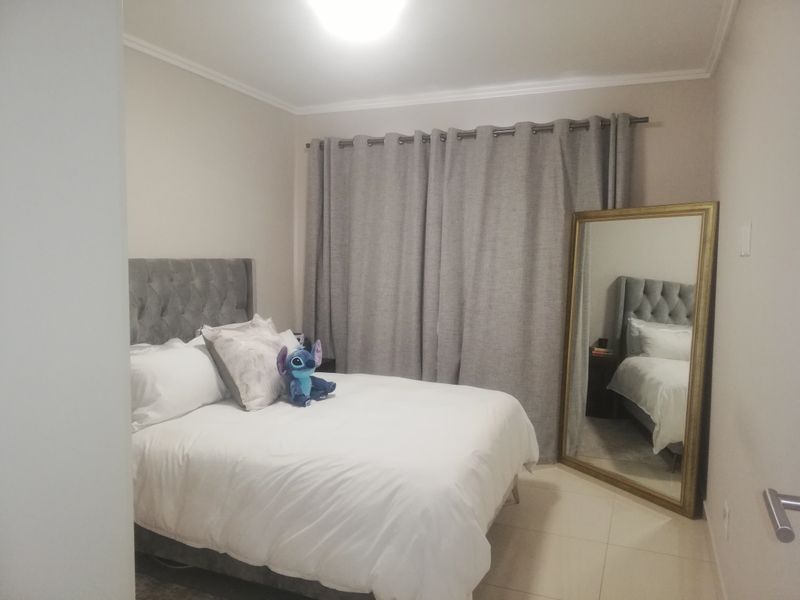 A well-maintained bedroom featuring neutral wall tones, tiled flooring, and floor-to-ceiling curtains.
