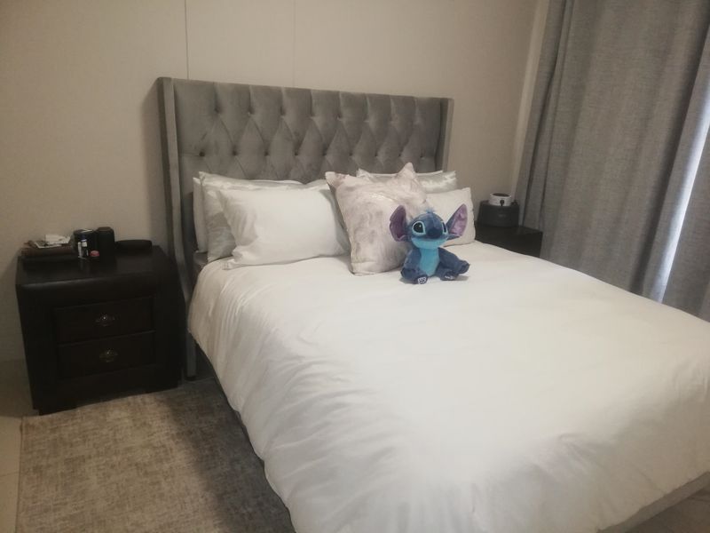 A cozy bedroom featuring a tufted grey headboard and neutral wall tones, providing a comfortable and inviting sleeping space.