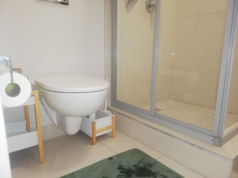 A functional bathroom featuring a wall-mounted toilet and a glass-enclosed shower with tiled finishes.