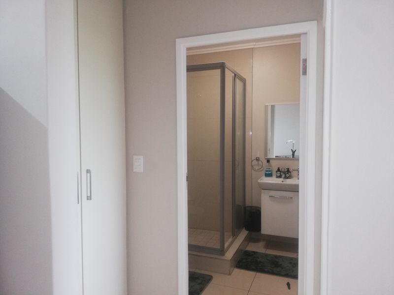 A clean and functional bathroom featuring a glass shower enclosure, a modern vanity basin, and adjacent built-in storage cupboards.