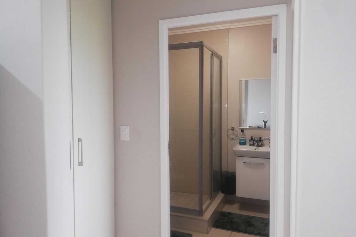 A clean and functional bathroom featuring a glass shower enclosure, a modern vanity basin, and adjacent built-in storage cupboards.