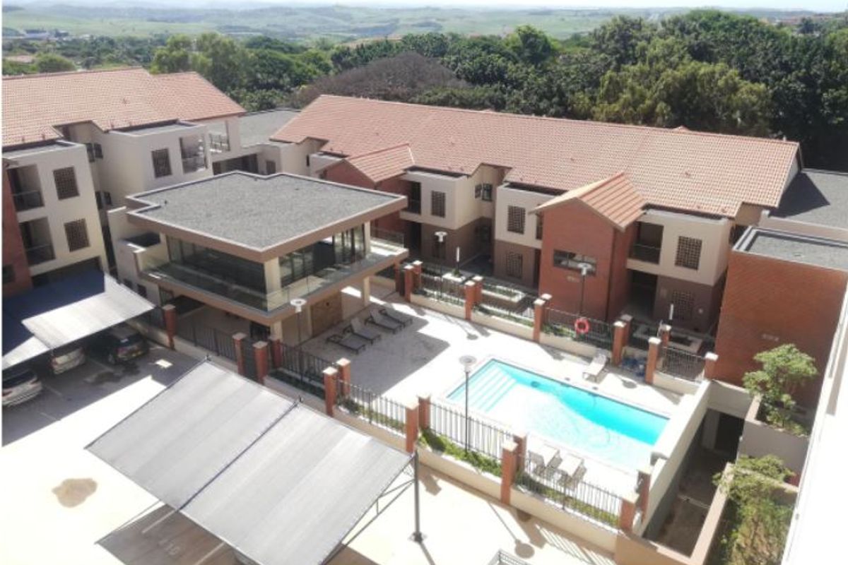 Aerial view of the apartment complex featuring a communal swimming pool, clubhouse, and covered parking facilities within a secure, landscaped estate.