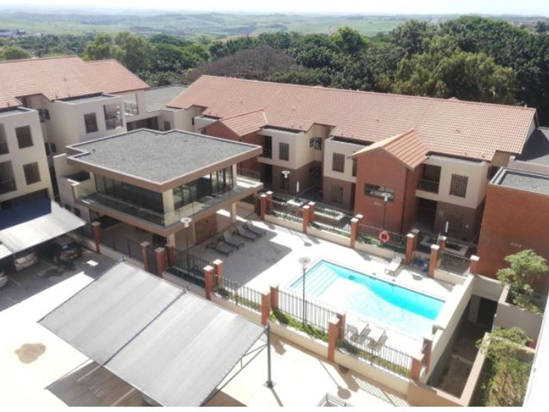 Aerial view of the apartment complex featuring a communal swimming pool, clubhouse, and covered parking facilities within a secure, landscaped estate.