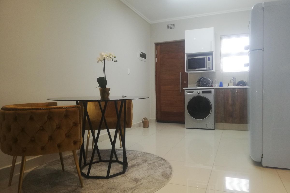 Open plan living area featuring a compact kitchen with built-in cabinetry, microwave, and tiled flooring, seamlessly connected to the dining space.