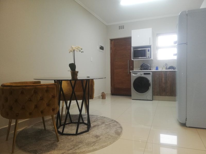 Open plan living area featuring a compact kitchen with built-in cabinetry, microwave, and tiled flooring, seamlessly connected to the dining space.