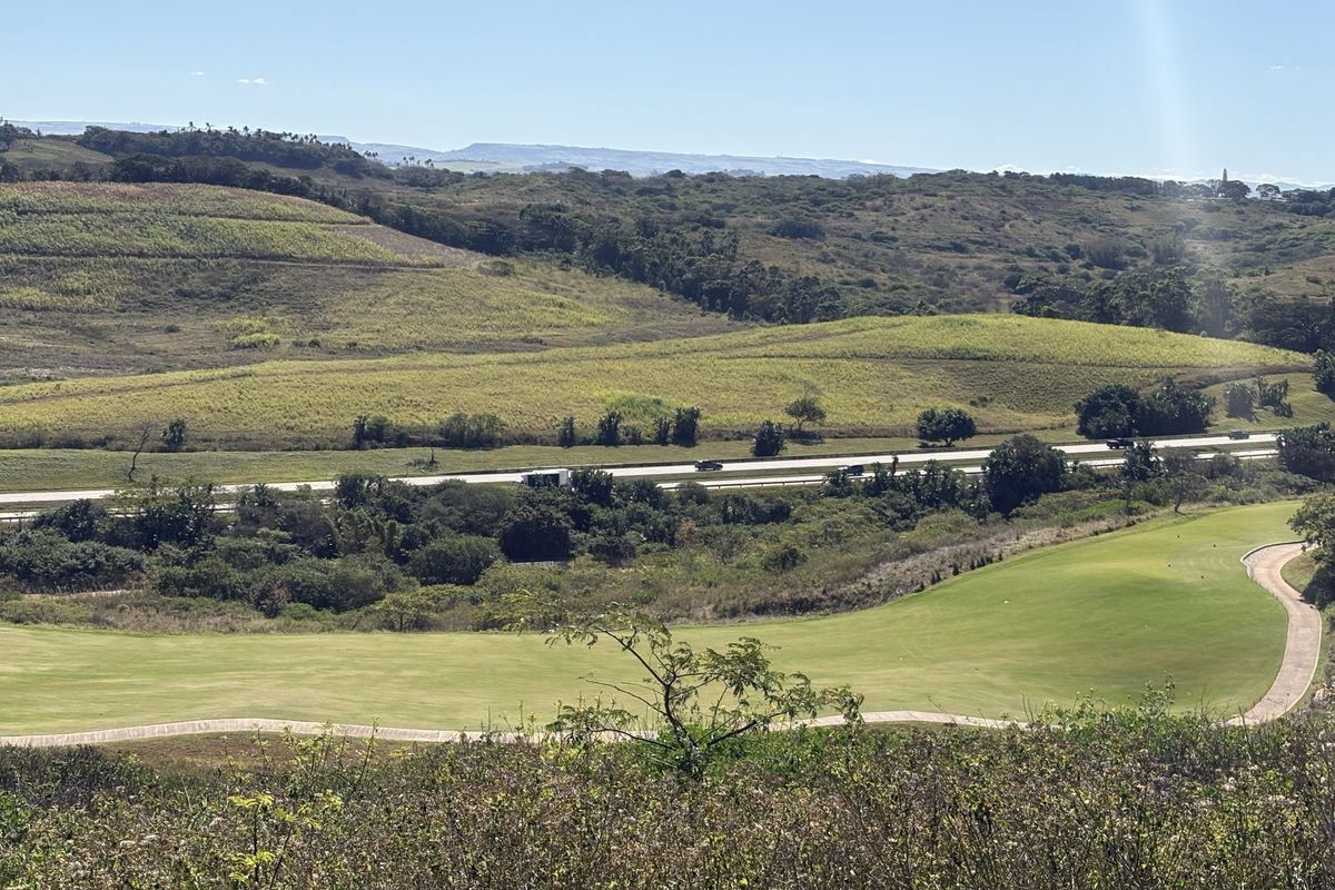 A scenic elevated view overlooking a manicured golf course fairway with a paved cart path and rolling hills in the background.