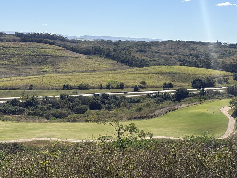 A scenic elevated view overlooking a manicured golf course fairway with a paved cart path and rolling hills in the background.